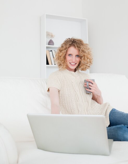 Hermosa mujer rubia relajante con su computadora portátil mientras está sentado en un sofá