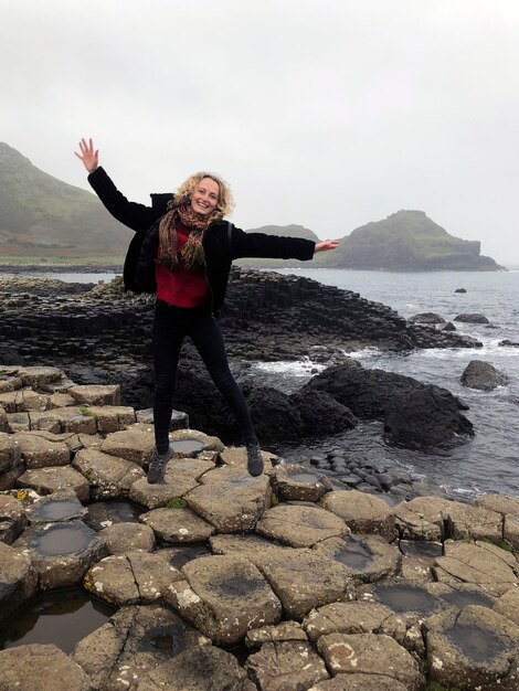 Hermosa mujer rubia salta por encima de las rocas de la atracción turística de Irlanda del Norte Calzada del Gigante