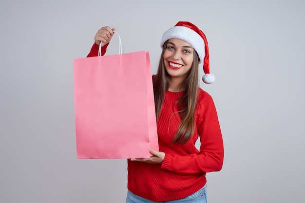 Hermosa mujer rubia con sombrero de santa, suéter rojo, tiene paquetes con compras. El concepto de ventas navideñas, compras, descuentos.