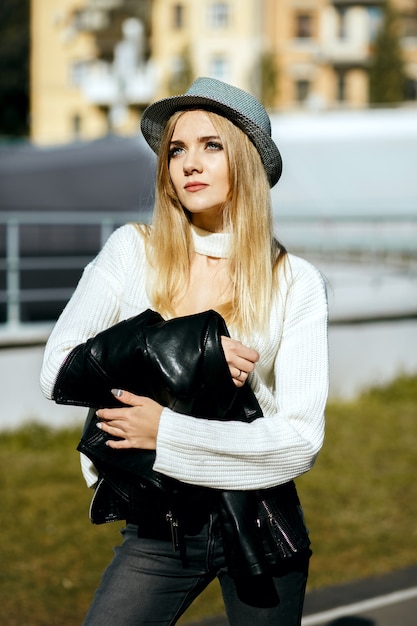 Hermosa mujer rubia con sombrero y suéter de punto, posando en un día soleado