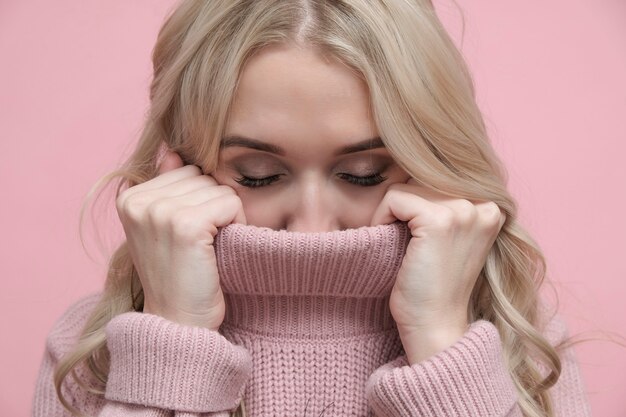 Hermosa mujer rubia en suave suéter rosa cálido cerró los ojos.