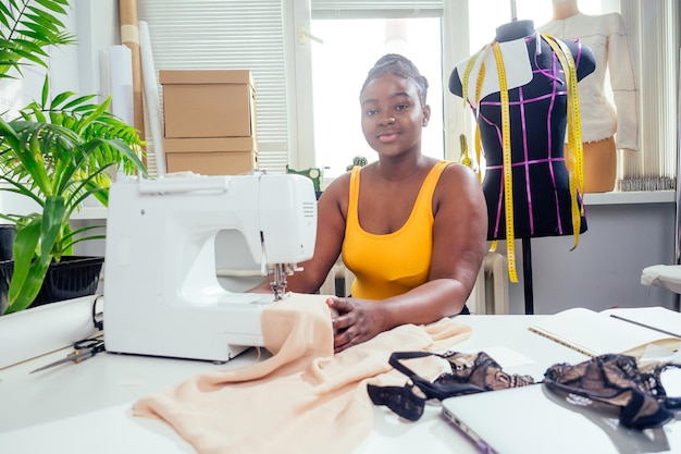 Hermosa mujer sastre afroamericana cosiendo cordones de lencería sexy en la sala de exposición.