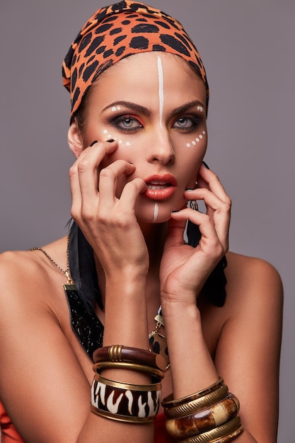 Hermosa mujer seductora con chal colorido en la cabeza y accesorios, posando con la mano en la cara y los labios. Aislado sobre fondo gris.