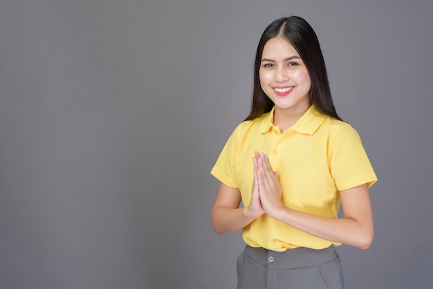 Hermosa mujer segura es saludo (Thai wai) para mostrar respeto sobre gris