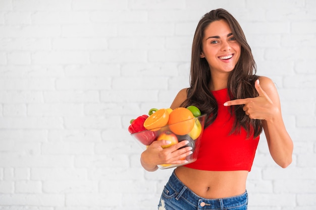 Hermosa mujer señalando verduras frescas y frutas en un tazón