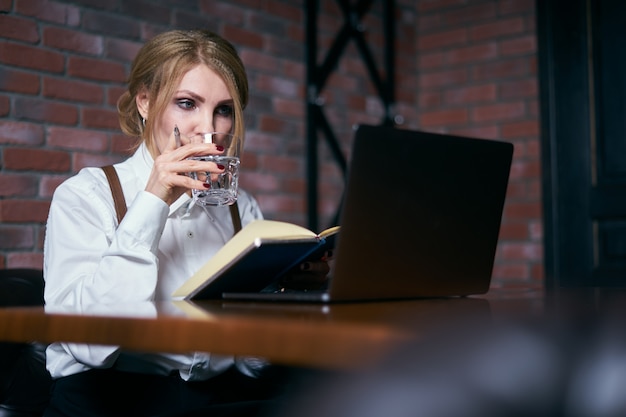 Hermosa mujer senior trabajando en café con laptop y escribiendo en el bloc de notas