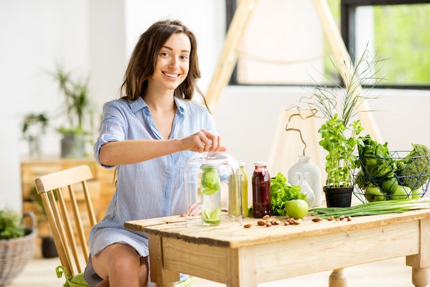 Hermosa mujer sentada con alimentos y bebidas verdes saludables en casa. Concepto de comida vegana y desintoxicación.