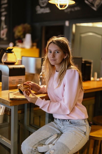 Una hermosa mujer sentada en un café, disfrutando de un croissant.