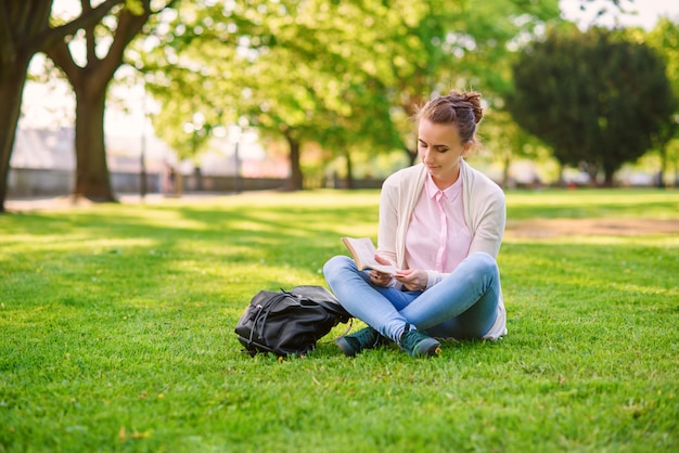 Hermosa mujer sentada en el césped y leyendo el libro en el parque en verano