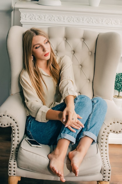 Hermosa mujer sentada Chica en una silla. La rubia se sentó en una silla o sofá en la sala de estar.