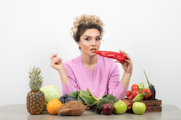 Foto hermosa mujer sentada a la mesa y sosteniendo ají rojo.