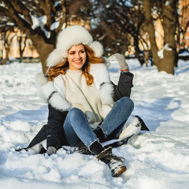 Hermosa mujer sentada en la nieve de invierno al aire libre