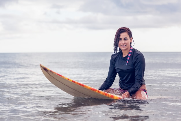 Hermosa mujer sentada en la tabla de surf en el agua