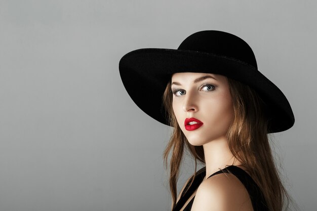 Hermosa mujer sexy con lápiz labial rojo en un sombrero negro