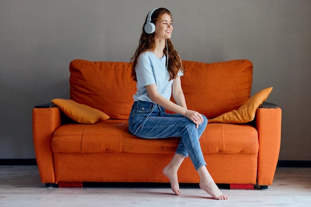 Hermosa mujer en el sofá naranja escuchando música con tecnologías de auriculares
