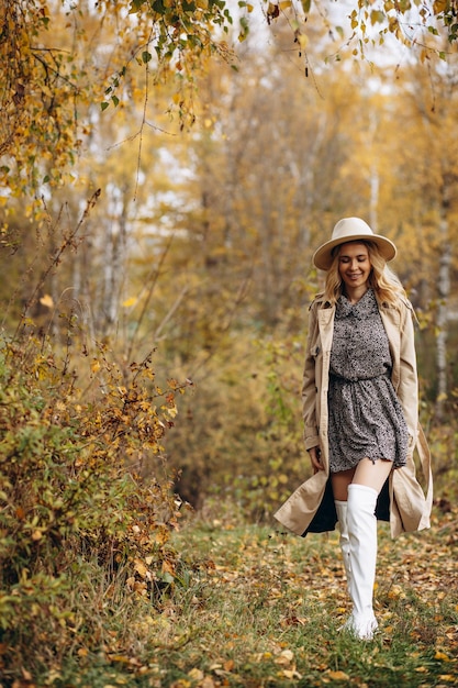 Hermosa mujer con sombrero y abrigo caminando en el parque de otoño