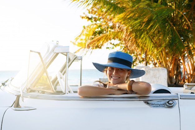 Hermosa mujer con sombrero azul y descapotable retro blanco