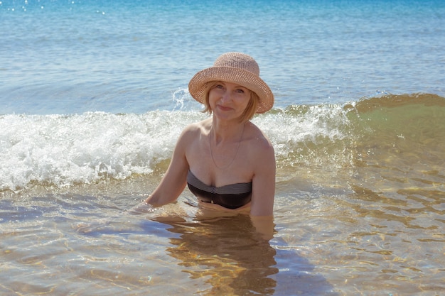 Hermosa mujer con sombrero y bikini en agua de mar sonriendo. Pasatiempo de verano y relajación.