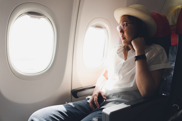 Hermosa mujer con un sombrero de paja usando un teléfono inteligente mientras está sentada en el avión