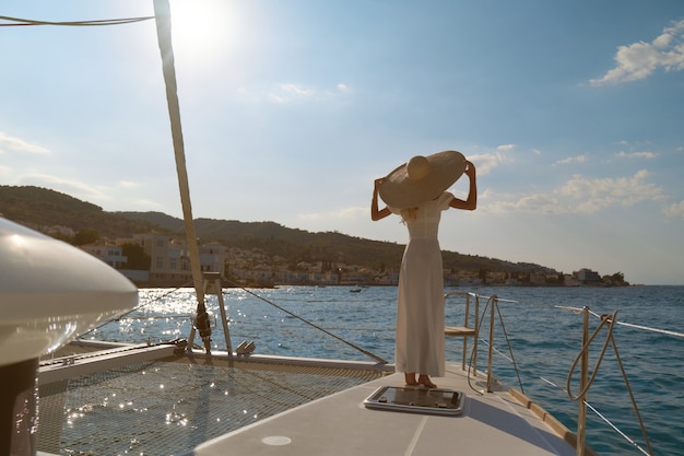 Hermosa mujer con sombrero de paja y vestido blanco en un yate disfruta del viaje, Spetses, Grecia, Europa.