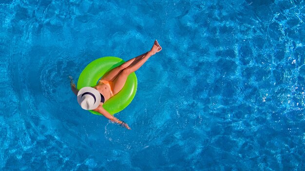 Hermosa mujer con sombrero en la piscina vista aérea desde arriba, la joven en bikini se relaja y nada en un anillo inflable y se divierte en el agua de vacaciones