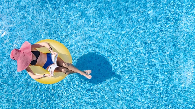 Hermosa mujer con sombrero en la piscina vista aérea superior desde arriba, joven en bikini se relaja y nada en un anillo inflable donut y se divierte en el agua, complejo de vacaciones tropical