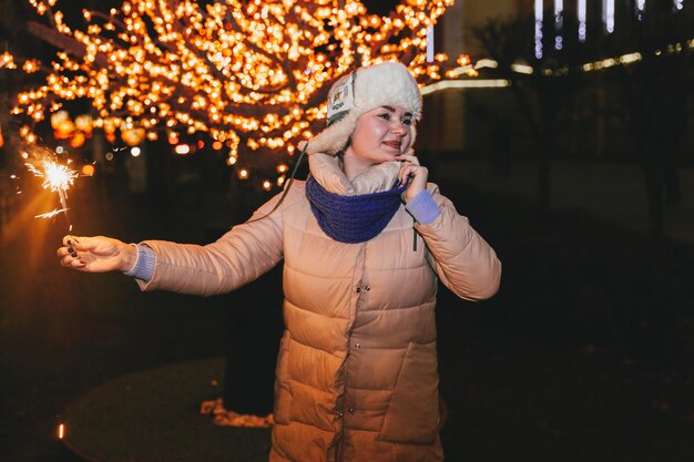 Hermosa mujer con un sombrero de punto y una bufanda de pie en la ciudad con una bengala. Concepto de celebración y Navidad.