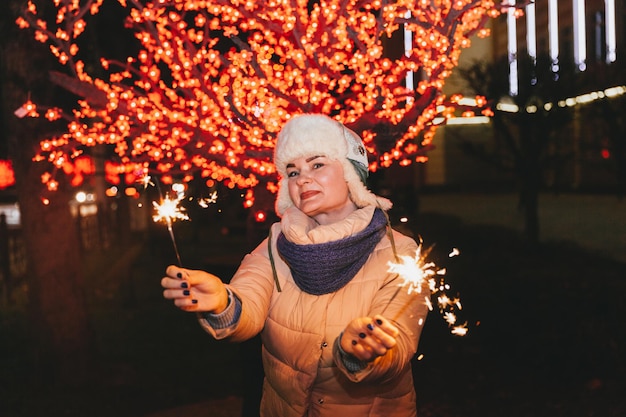 Hermosa mujer con un sombrero de punto y una bufanda de pie en la ciudad con una bengala. Concepto de celebración y Navidad.