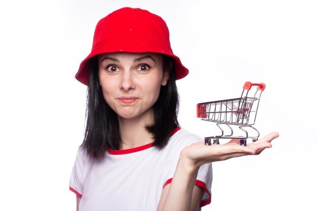 Foto hermosa mujer con un sombrero rojo de panamá sostiene un pequeño carrito de compras