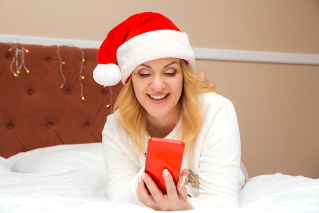 Hermosa mujer con sombrero de santa claus posando con un teléfono en sus manos