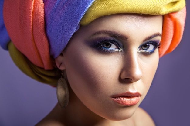 Hermosa mujer con sombreros de colores y maquillaje azul, Foto de estudio sobre fondo púrpura