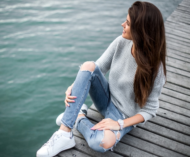 Hermosa mujer soñando sentado en el muelle junto al lago.