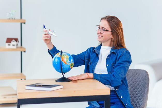 Hermosa mujer soñando con vacaciones. Niña sostiene en la mano un modelo de avión y vuela alrededor de globo pequeño.