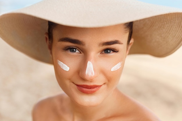 Foto hermosa mujer sonríe aplicando crema solar en la cara cuidado de la piel y el cuerpo protección solar