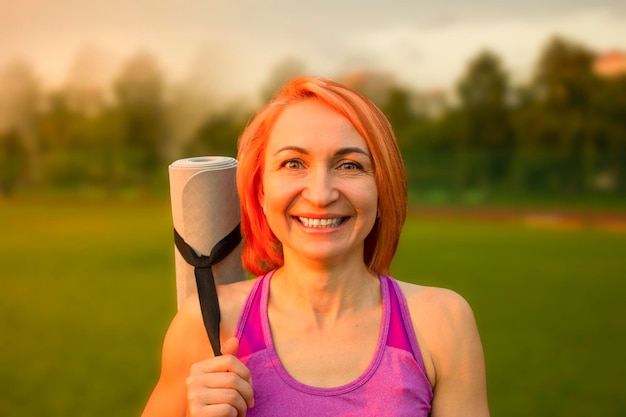 Hermosa mujer sonriendo con una alfombra de yoga en el fondo del parque