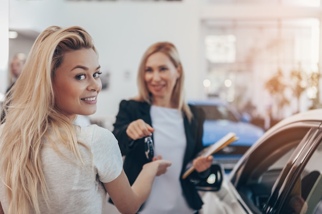 Hermosa mujer sonriendo a la cámara recibiendo las llaves del auto a su nuevo automóvil en concesionario.