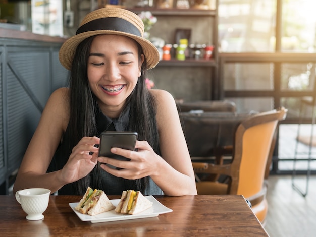 Hermosa mujer sonriendo mientras usa en el teléfono móvil en la cafetería.