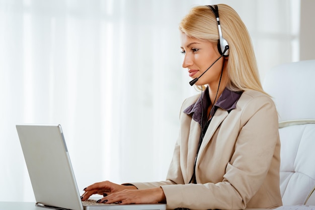 Hermosa mujer sonriente con un auricular en la cabeza usando una laptop en la oficina.