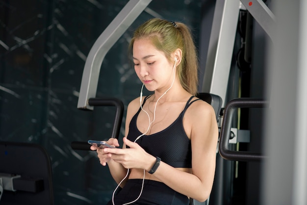 Una hermosa mujer sonriente en auriculares usando una red social y escuchando música en el concepto de gimnasio, fitness y tecnología