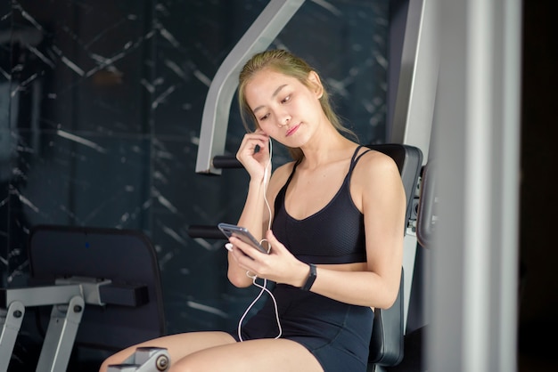 Una hermosa mujer sonriente en auriculares usando una red social y escuchando música en el concepto de gimnasio, fitness y tecnología