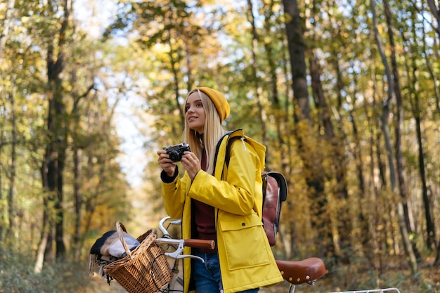 Hermosa mujer sonriente en bicicleta en el bosque de otoño Fotógrafo tomando fotografías en el parque