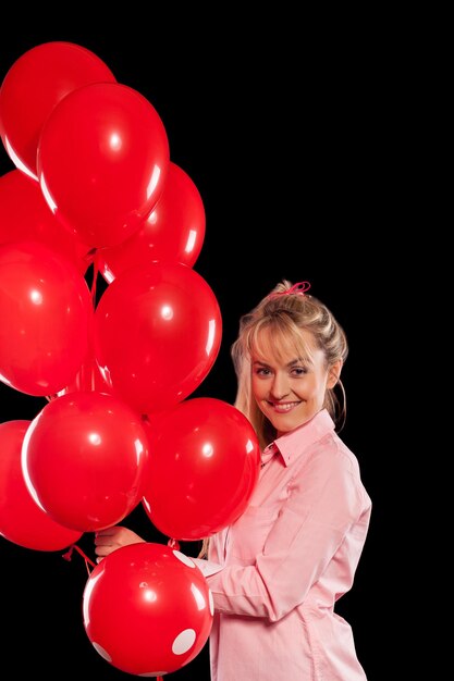 Hermosa mujer sonriente en blusa rosa sosteniendo globos rojos sobre fondo negro