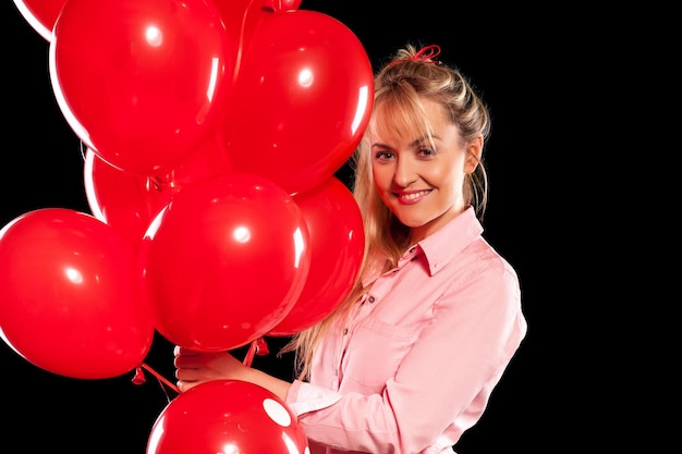 Hermosa mujer sonriente en blusa rosa sosteniendo globos rojos sobre fondo negro