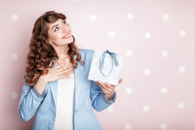 Foto hermosa mujer sonriente en chaqueta azul tiene caja de regalo con pelo rizado