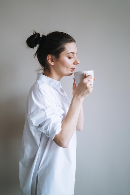 Hermosa mujer sonriente estudiante adolescente con cabello largo oscuro en ropa de casa con la taza de café o té de la mañana