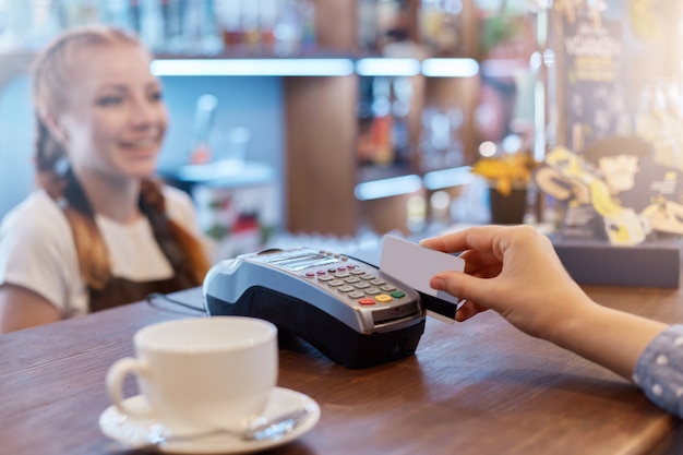 Hermosa mujer sonriente habla con el cliente que paga por terminal al sistema de tarjeta de crédito