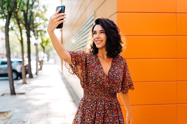 Hermosa mujer sonriente linda está utilizando teléfonos inteligentes en la calle dando un paseo en un día de verano