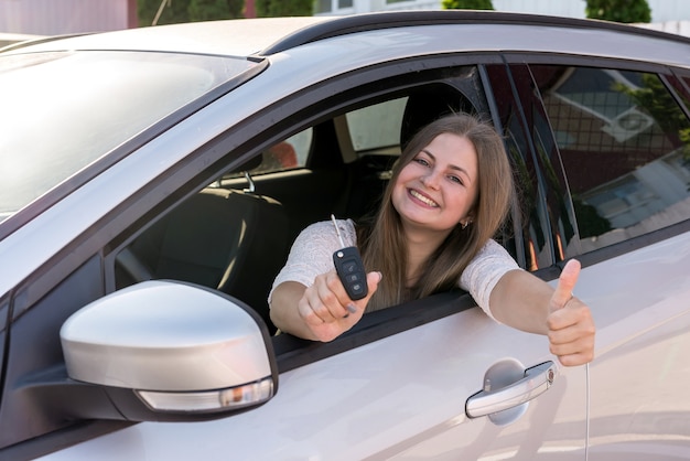 Hermosa mujer sonriente mostrando la llave del coche a través de la ventana