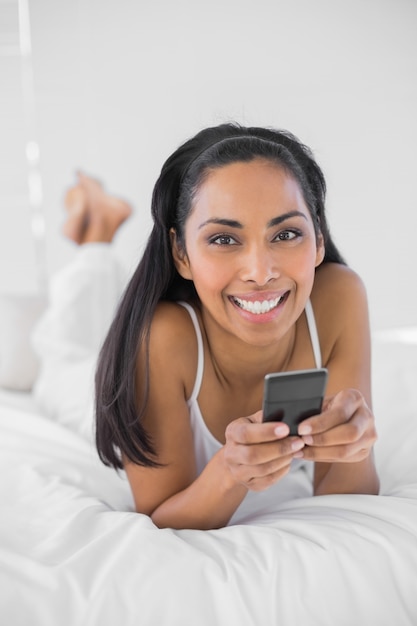 Hermosa mujer sonriente sosteniendo su teléfono inteligente sonriendo a la cámara