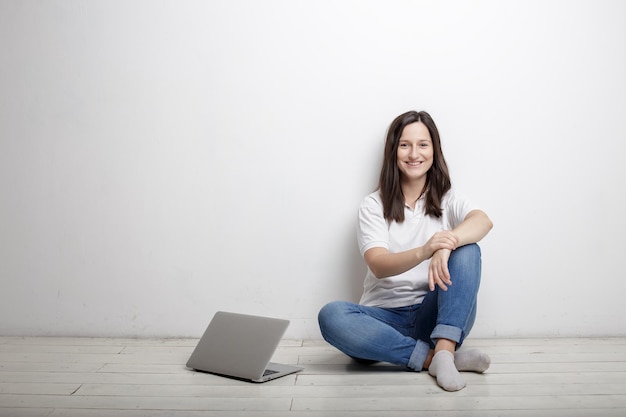 Hermosa mujer sonriente tiene un descanso del trabajo feliz sentada junto a la pared en el piso junto al cuaderno abierto